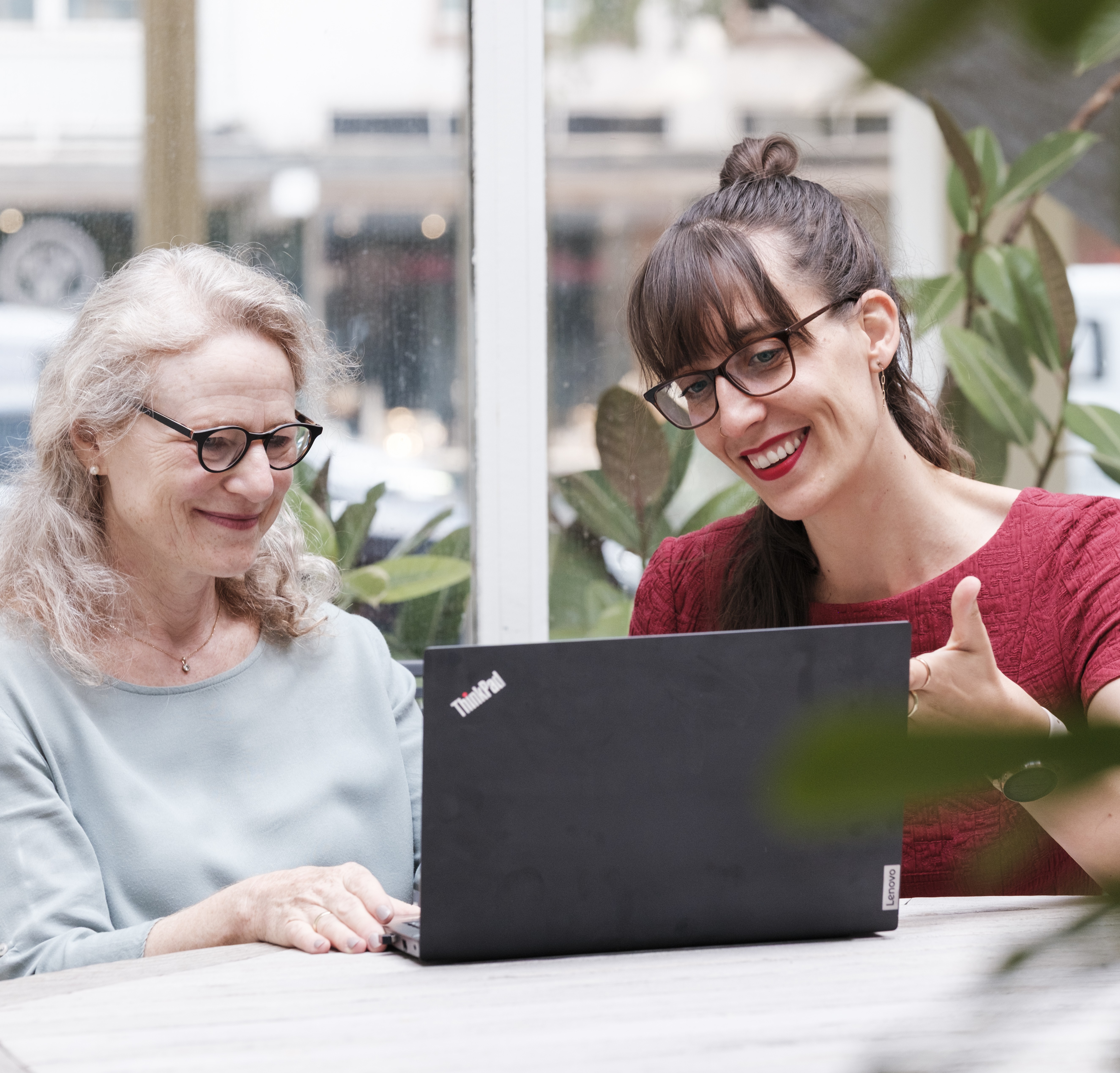 Zwei Frauen sitzen vor einem Laptop in einem Innenhof.
