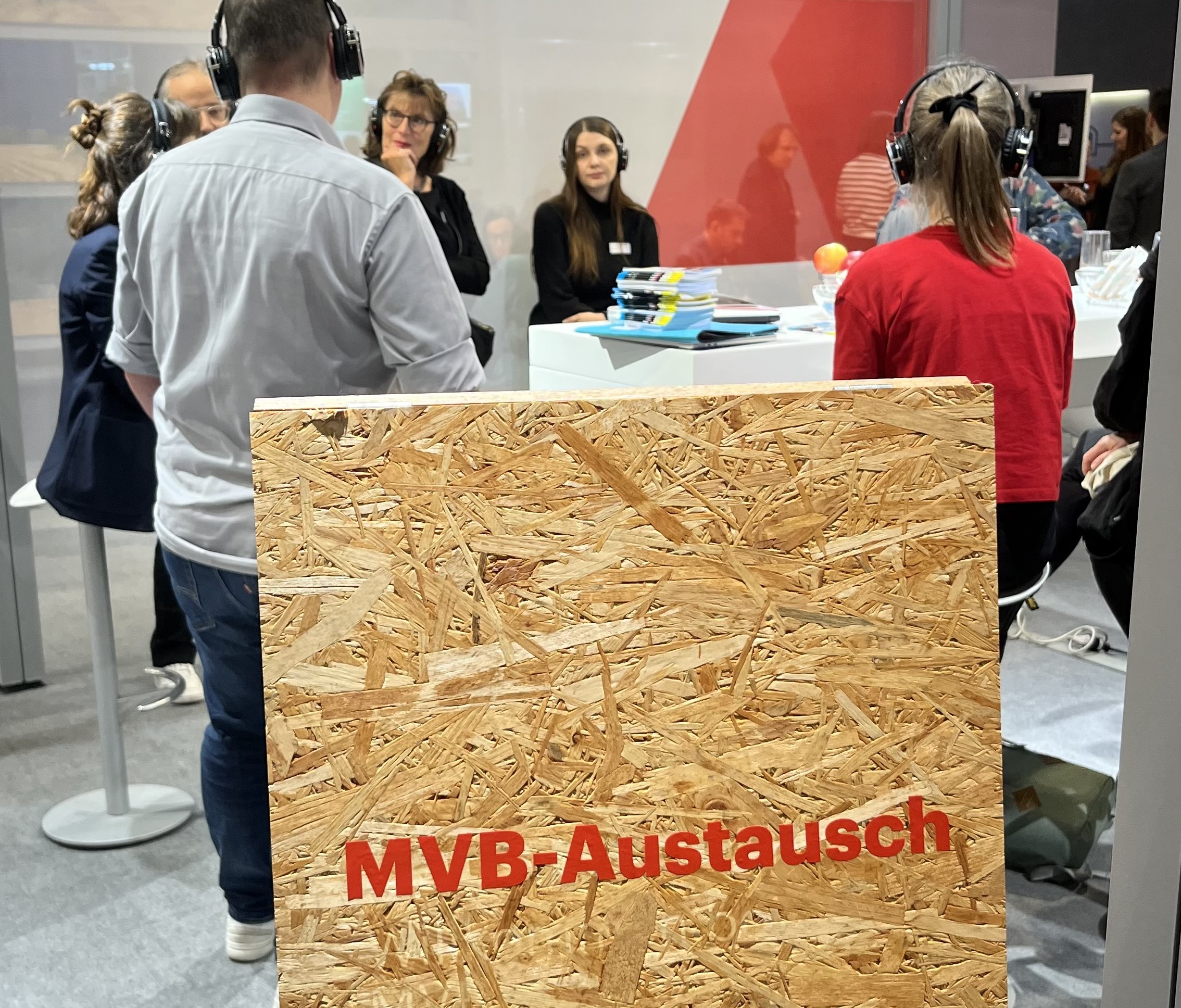 Holzschild mit der Aufschrift "MVB-Austausch" vor einer Gruppe Menschen.