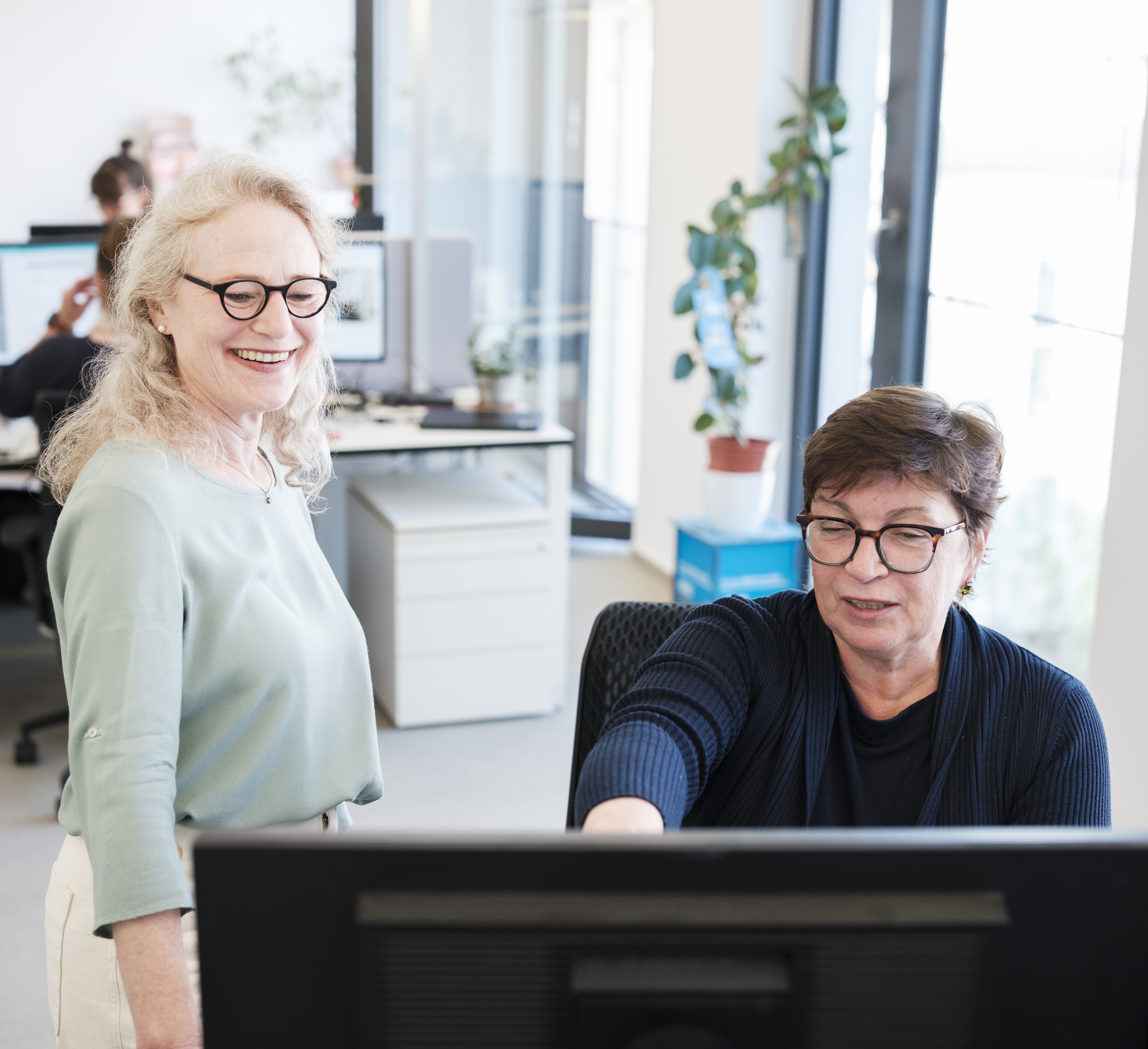 Zwei Frauen sitzen vor einem Computer im Büro.