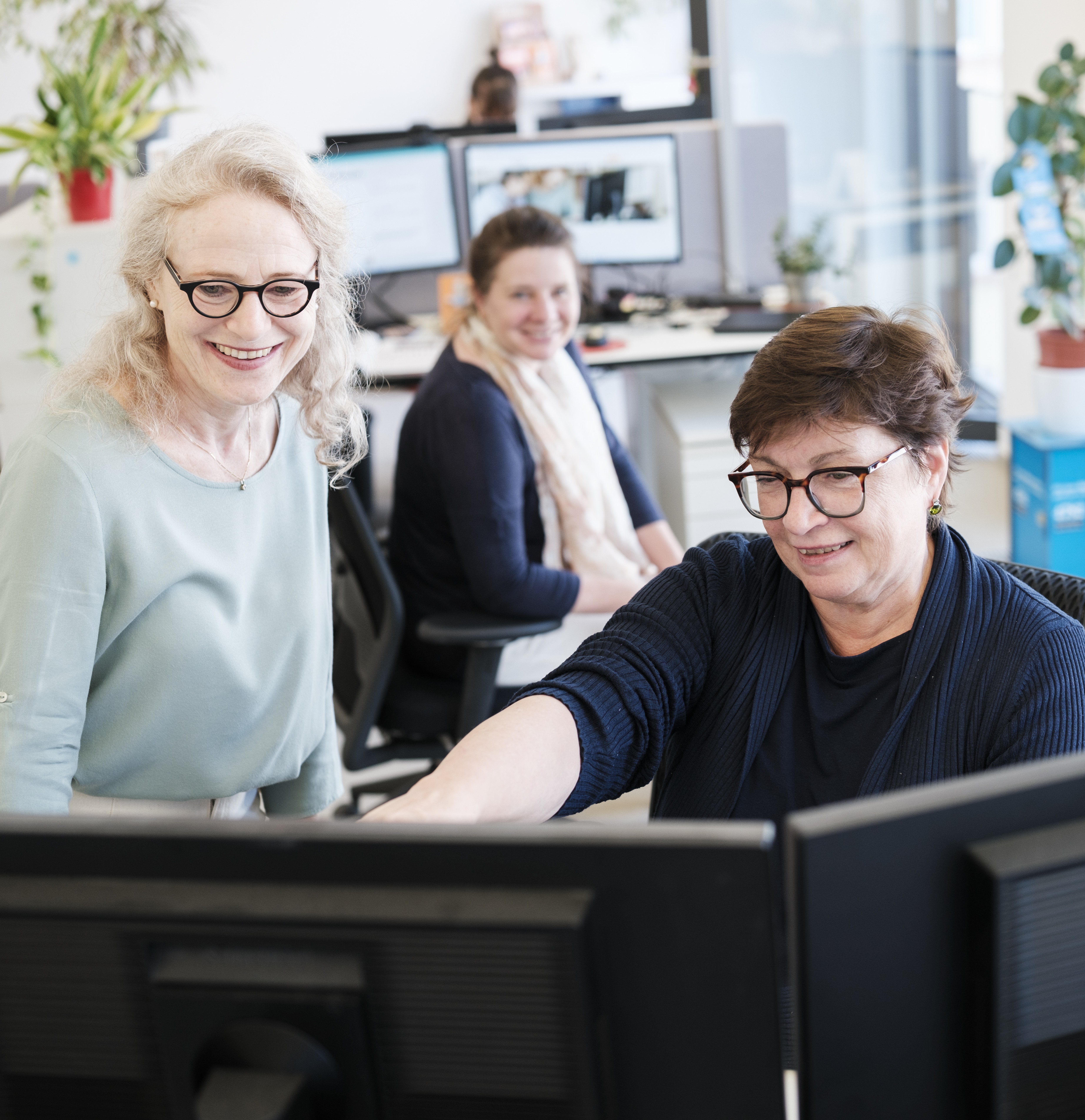 Drei lächelnde Frauen blicken auf einen PC-Bildschirm.