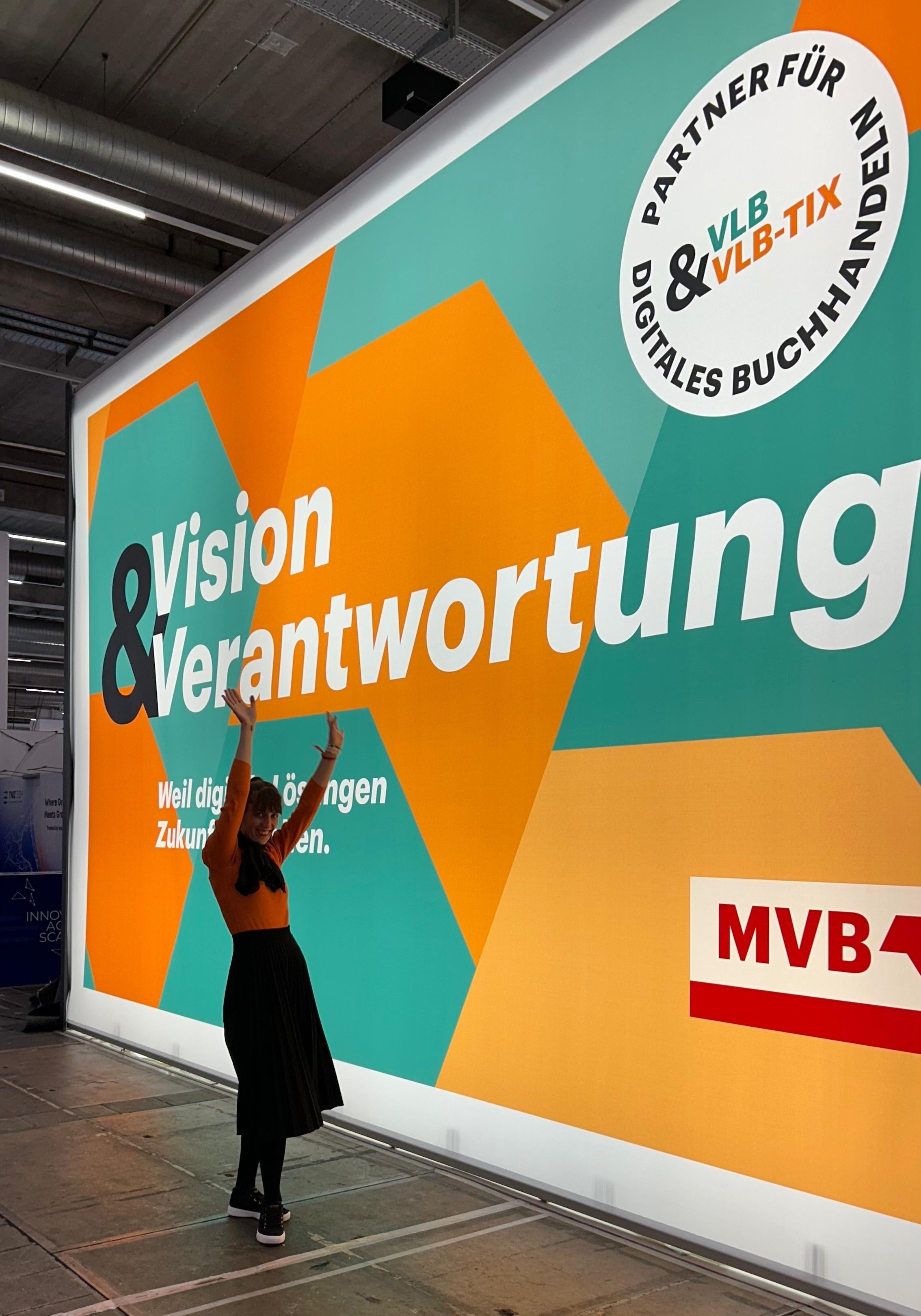 Eine Frau steht jubelnd vor einer Messewand mit der Aufschrift Vision und Verantwortung.