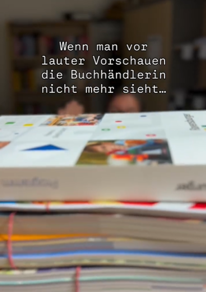 Frau winkt hinter einem Stapel Vorschauen.